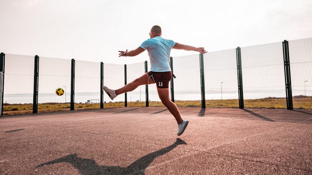 man kicking the yellow ball during daytime